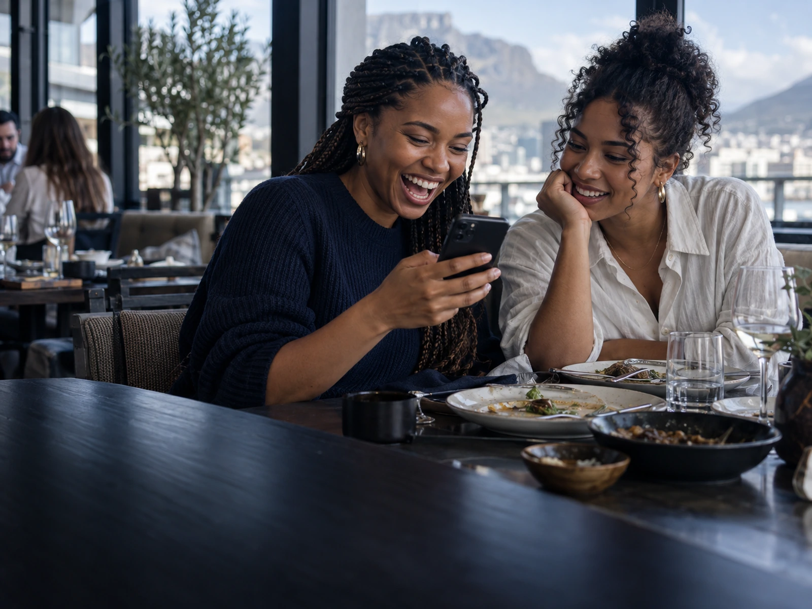 Two friends laughing at a phone over a meal