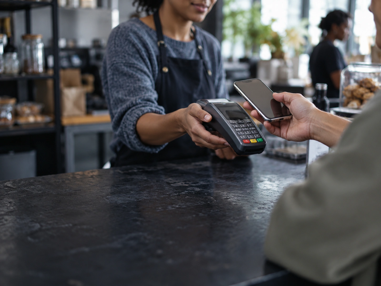A customer holding a phone out to a cashier at a till